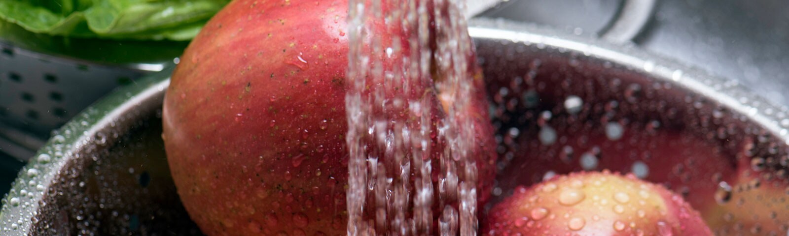 Washing red apples in a metal bowl with running water