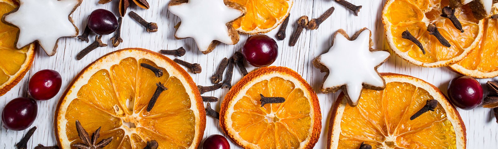 Rustic white, wood background covered with dried orange slices, berries, cinnamon sticks and cloves Rustic white, wood background covered with dried orange slices, berries, cinnamon sticks and cloves