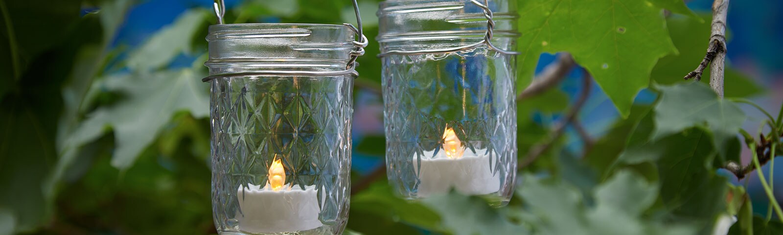 Two mason jars hanging from a tree, each one filled with a small LED candle