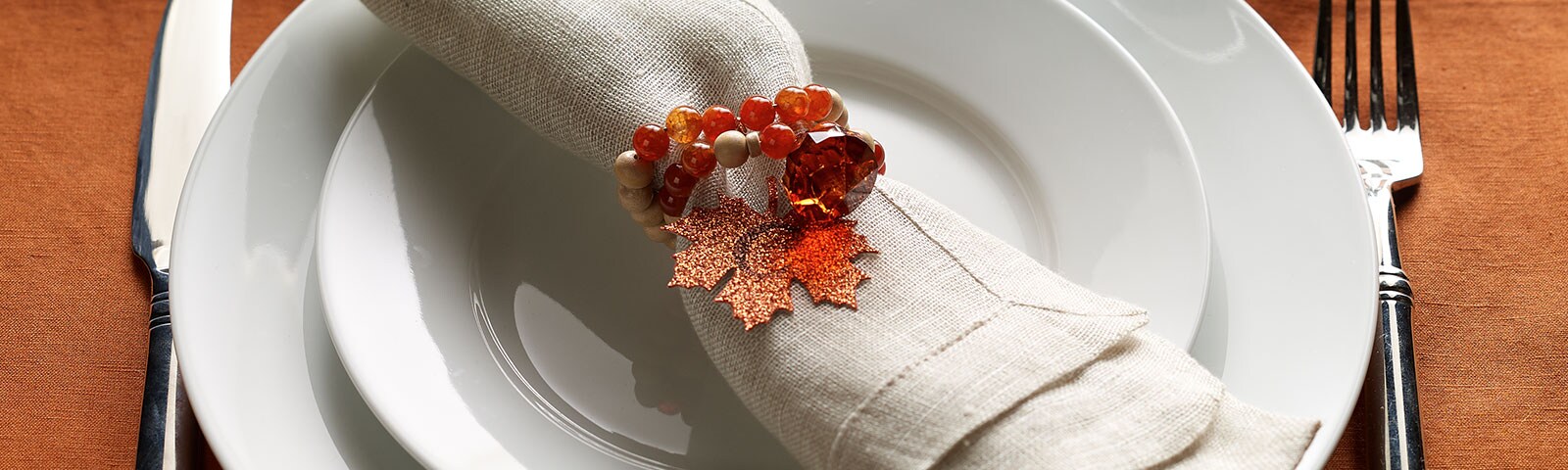 A table setting complete with a knife, fork, salad plate, dinner plate and linen napkin embellished with an ornate autumn napkin ring A table setting complete with a knife, fork, salad plate, dinner plate and linen napkin embellished with an ornate autumn napkin ring