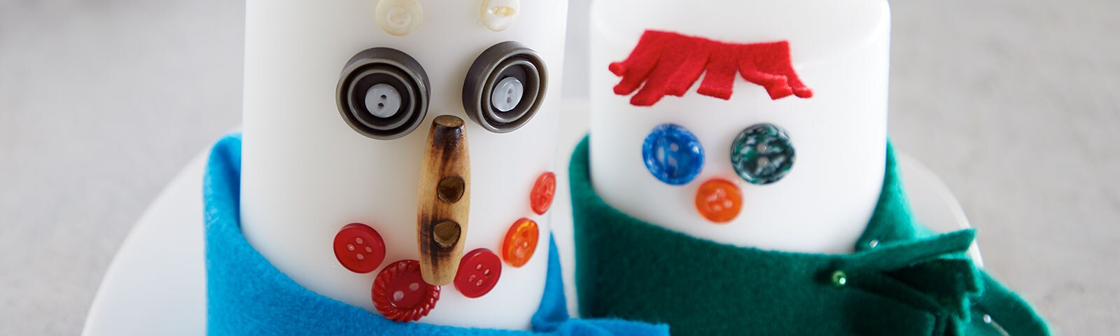 2 candles, each uniquely decorated with buttons and other craft items to look like snowmen wearing scarves 2 candles, each uniquely decorated with buttons and other craft items to look like snowmen wearing scarves