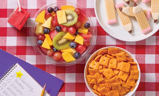 Picnic spread with fresh fruit, home-work, juice boxes, cheese crackers and vanilla wafer cookies shaped like pencils