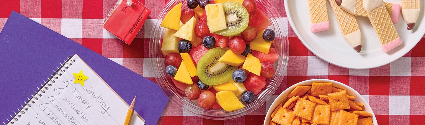 Picnic spread with fresh fruit, homework, juice boxes, cheese crackers and vanilla wafer cookies shaped like pencils