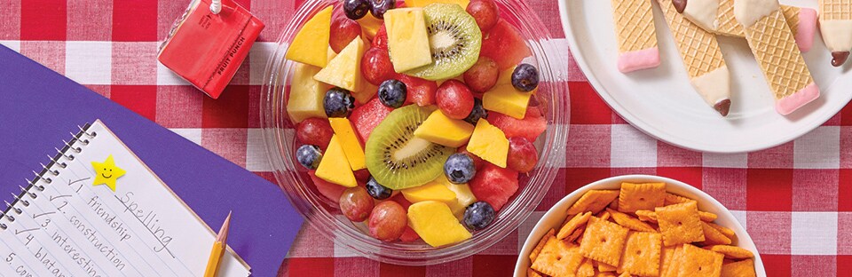 Picnic spread with fresh fruit, homework, juice boxes, cheese crackers and vanilla wafer cookies shaped like pencils
