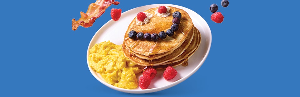 pancake stack with smiley face made with berries and bacon and eggs on the side